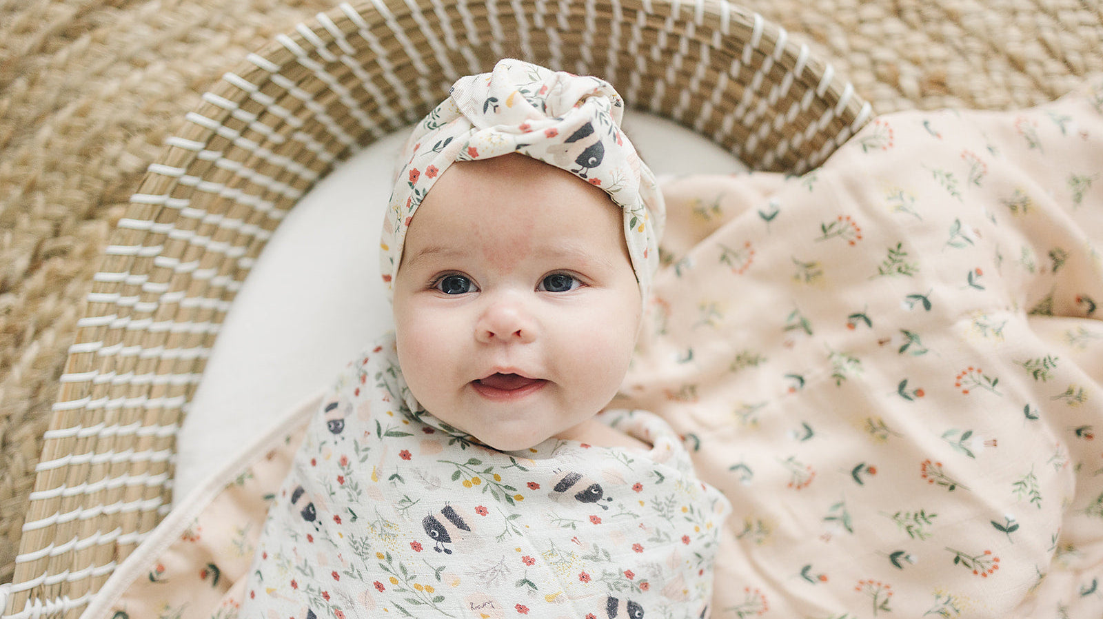 Baby wrapped in a bumblebee print swaddle, with a matching bumblebee headband, lying in a wicker basket